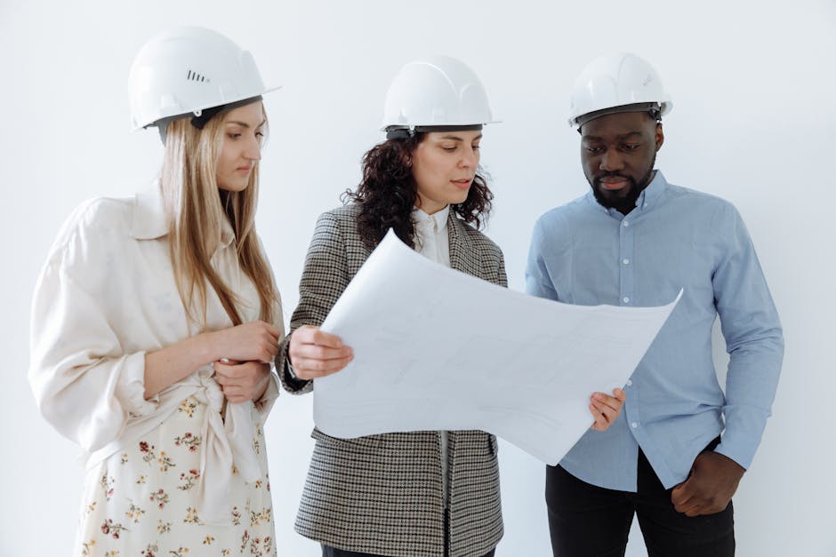 Three architects wearing hard hats reviewing blueprints indoors for a construction project.